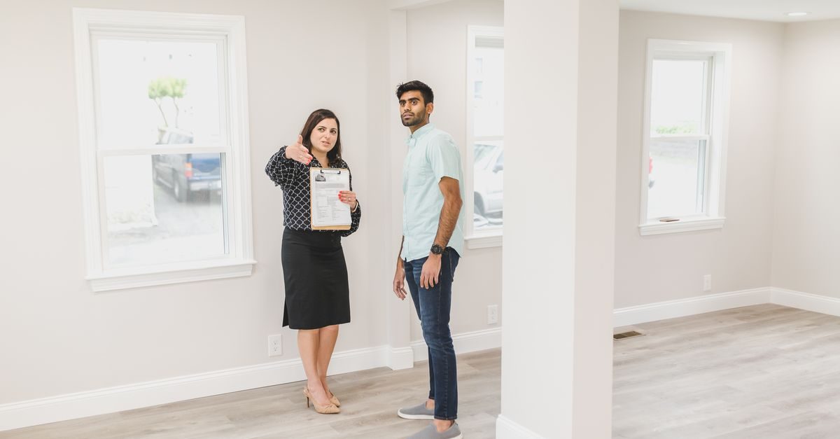 Eine Immobilienmaklerin zeigt einem Interessenten in einem hellen, leeren Raum eine Wohnung und hält ein Klemmbrett in der Hand