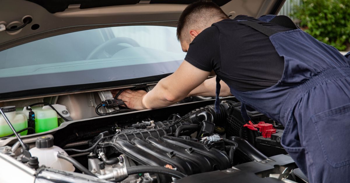 Un mécanicien en bleu de travail répare le moteur d'une voiture dans un garage automobile