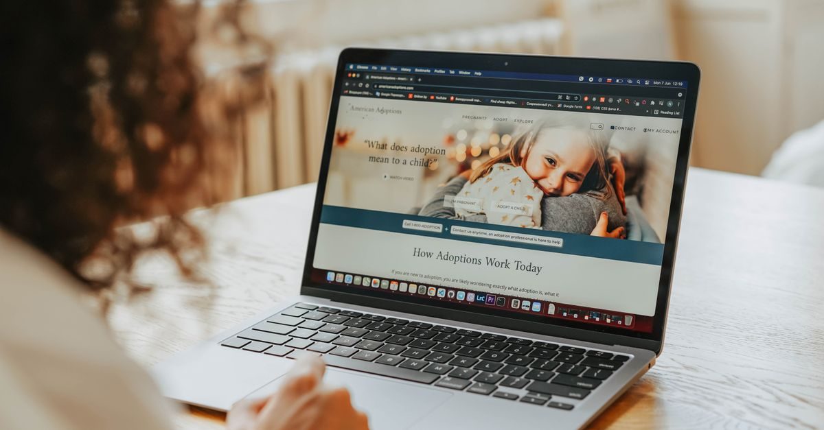 Person betrachtet an einem Laptop eine Website zum Thema Adoption mit einem Foto eines Kindes im Arm einer Person