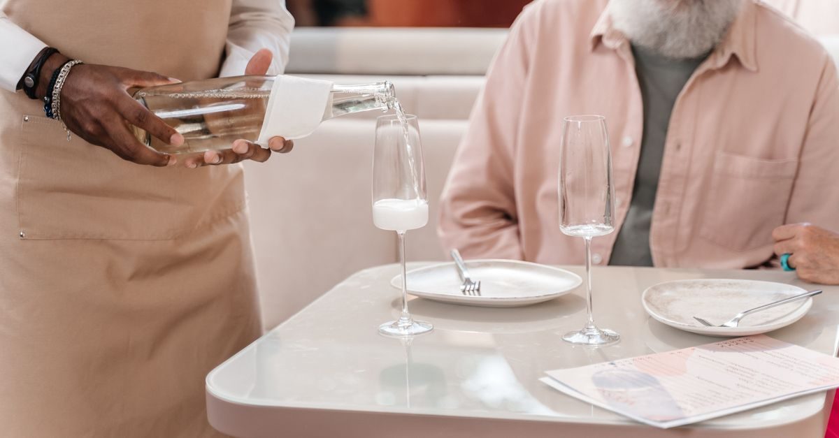 Eine Bedienung schenkt in einem Restaurant Wasser in ein Glas ein, während ein Gast am Tisch wartet
