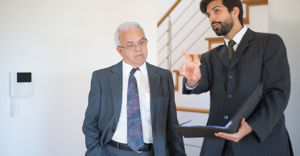 Agente immobiliare in giacca e cravatta mostra una casa a un cliente anziano durante una visita professionale in interni