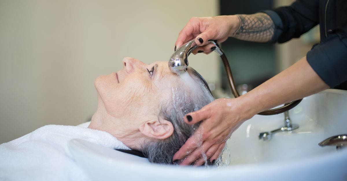 Peluquera lava el cabello a una mujer mayor en un salón de belleza con un ambiente relajado y profesional
