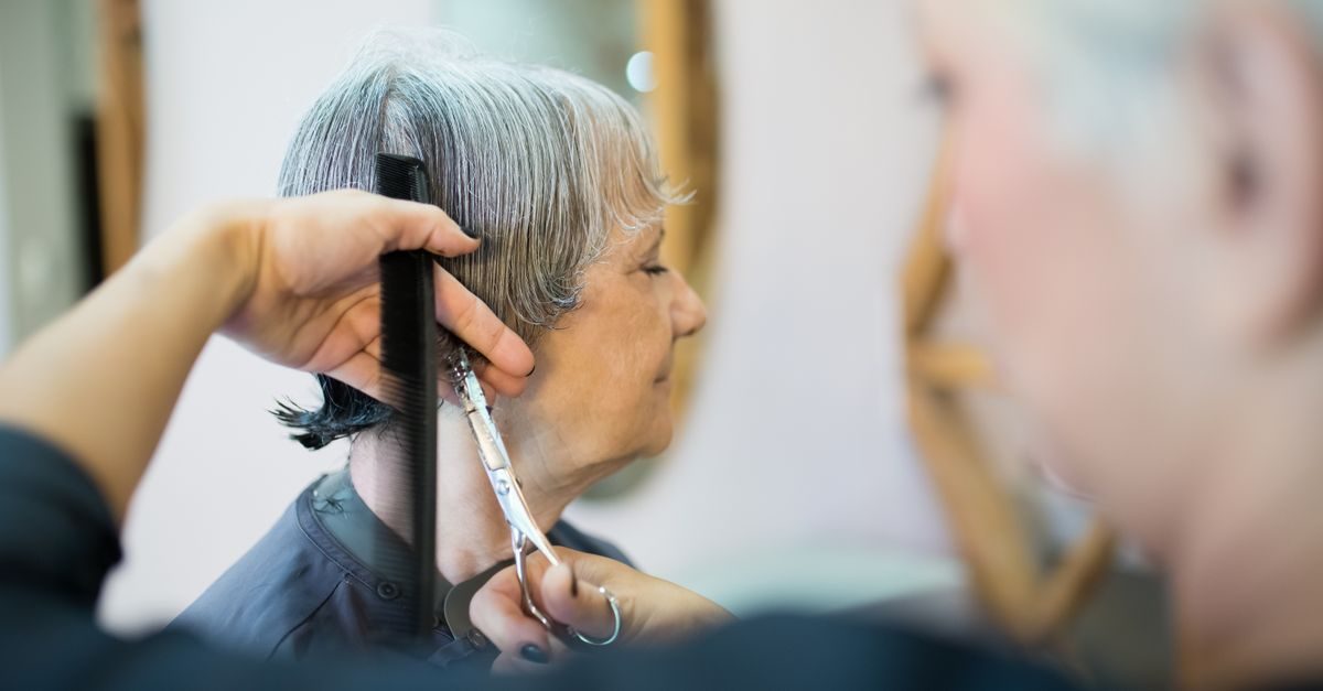 A hairstylist uses scissors and a comb to trim the gray hair of a woman in a salon setting