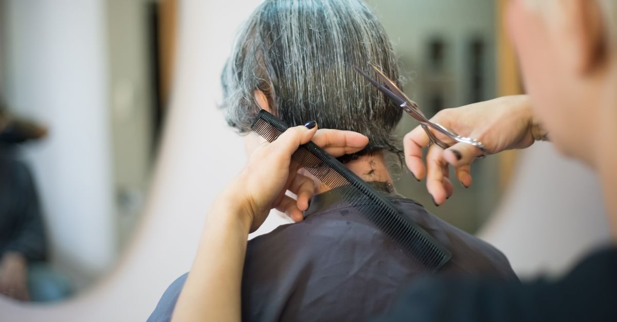 Kapper knipt het grijze haar van een klant met een schaar en kam in een professionele salon