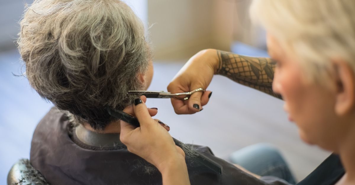 Peluquera con tatuaje en el brazo corta el cabello a una clienta de pelo canoso en un salón de belleza profesional