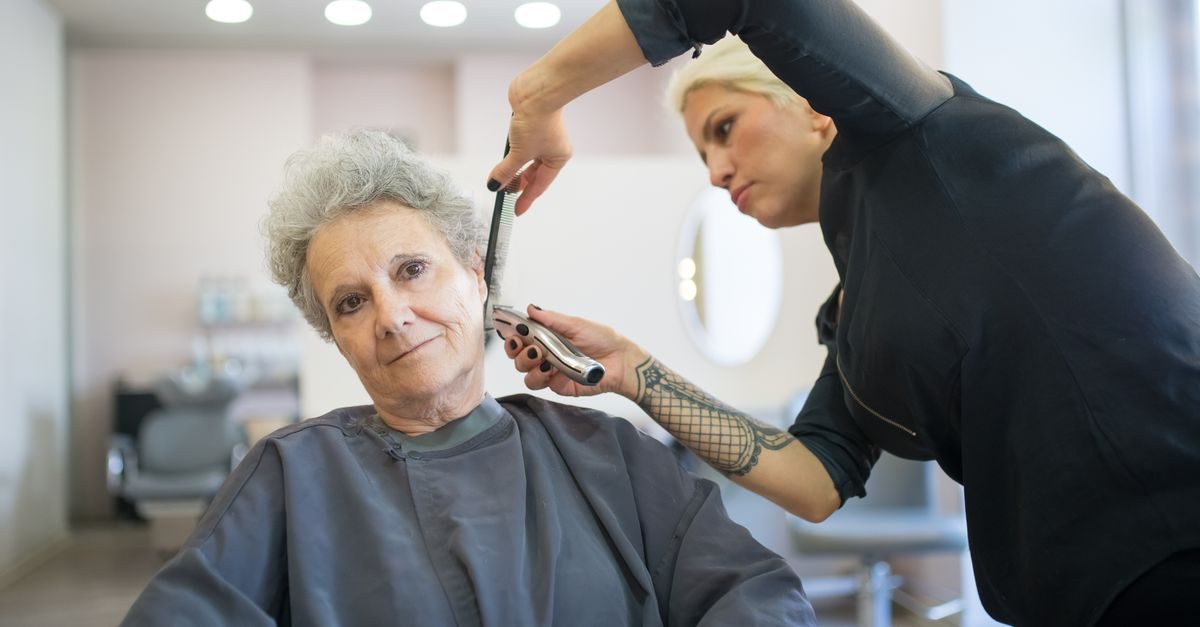 Fryzjerka z tatuażem na ręce strzyże maszynką włosy starszej klientce w profesjonalnym salonie fryzjerskim