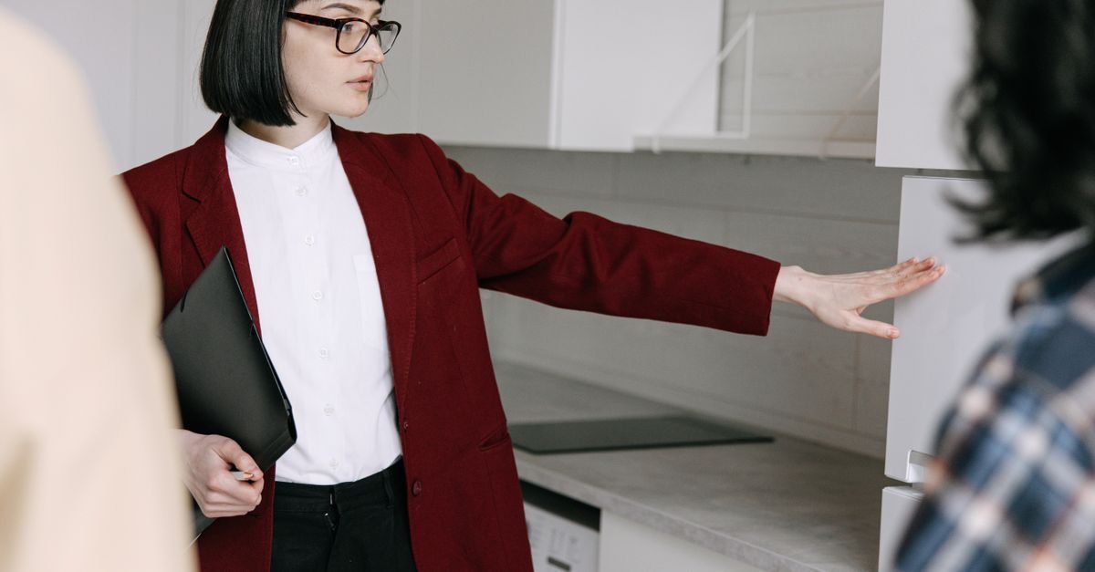 Agente immobiliare in giacca bordeaux mostra una cucina moderna a due potenziali clienti durante una visita professionale
