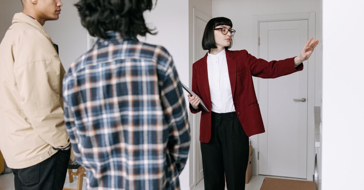 Une agente immobilière en veste rouge présente un appartement à un couple lors d'une visite professionnelle dans un intérieur