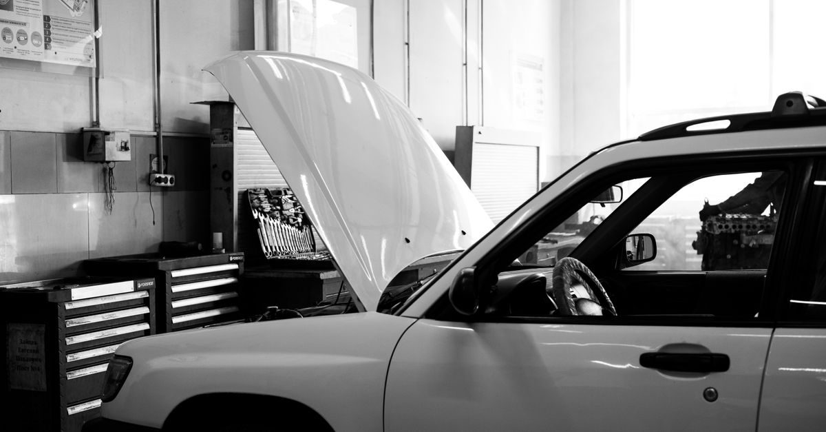 Auto con cofano aperto in un'officina meccanica attrezzata con cassettiere e attrezzi in bianco e nero