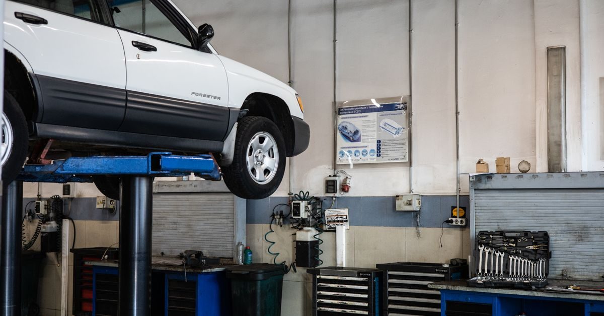 White car raised on a hydraulic lift inside a professional automotive repair garage with tools and equipment visible