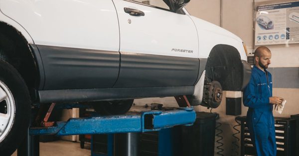 Monteur in blauwe overall staat naast een witte auto op een hefbrug in een garage